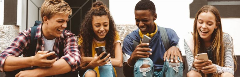 Four teenagers sitting together, looking at their cell phones.